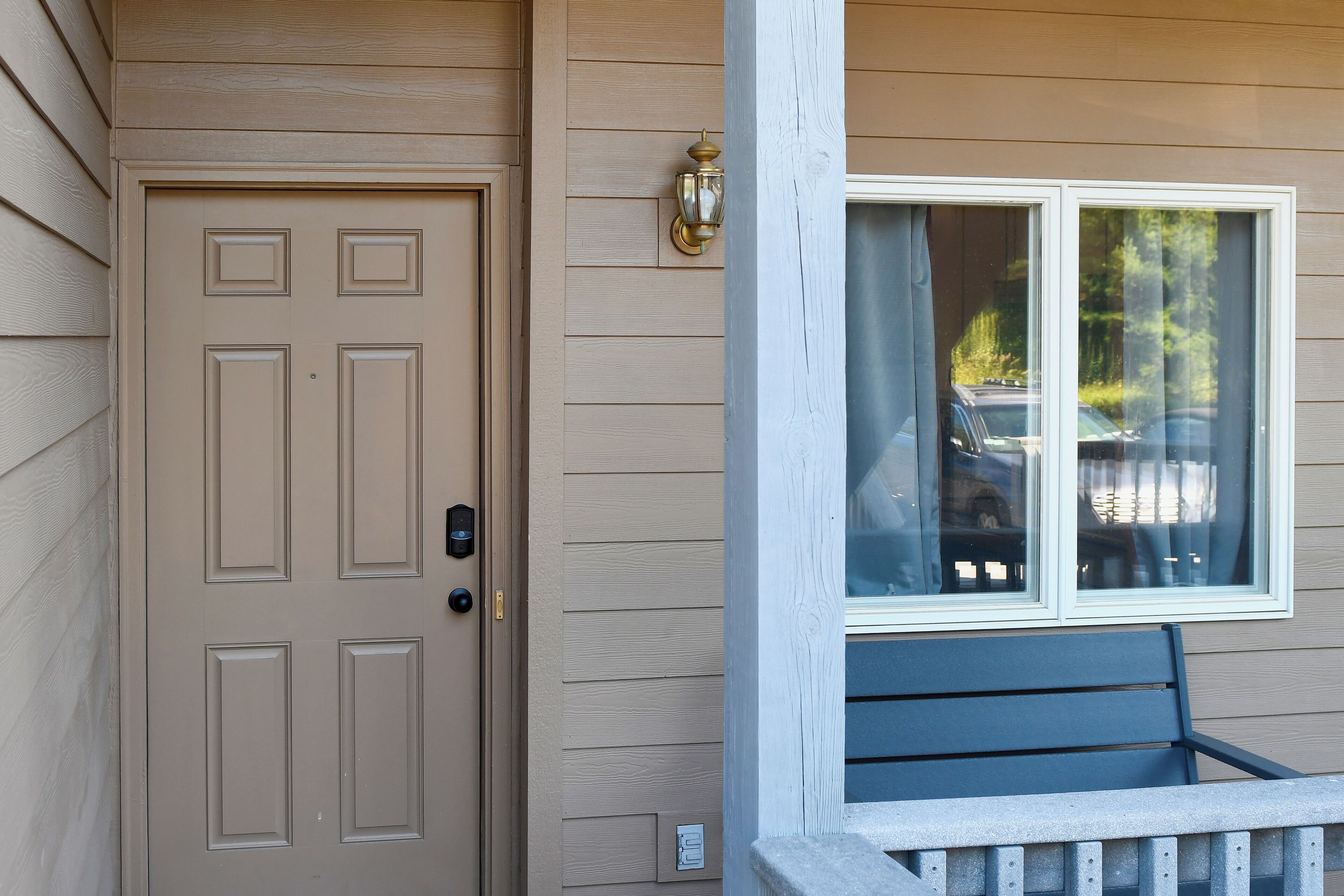 A beige door with a keypad lock, a window with a view of parked cars, and a bench outside.