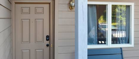 A beige door with a keypad lock, a window with a view of parked cars, and a bench outside.