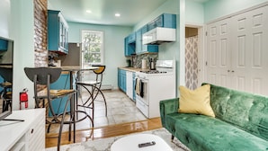 A compact kitchen with a dining area, a sofa, and a remote control on a coffee table. - Walk to Hblr & Liberty State Park: Jersey City Apt (Jersey City)