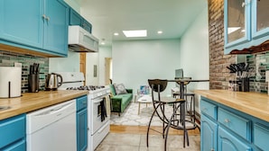 A compact kitchen with teal cabinetry, a white stove, and a dining area with a table and chairs. - Walk to Hblr & Liberty State Park: Jersey City Apt (Jersey City)