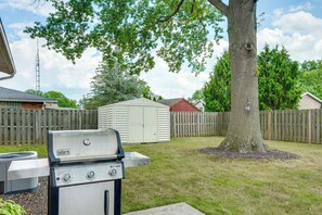 Ein Garten mit einem Weber Spirit Grill, einem Holzzaun und einem Gartenhaus.