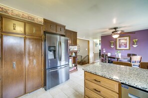 A kitchen with wooden cabinets, a stainless steel refrigerator, granite countertops, and a dining area with a purple wall. - Hot Tub, Gym & Office! Family Home in Massillon (Massillon)