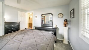Une chambre à coucher comprenant un lit, une commode, un miroir, une horloge et un casque décoratif posé sur un piédestal.