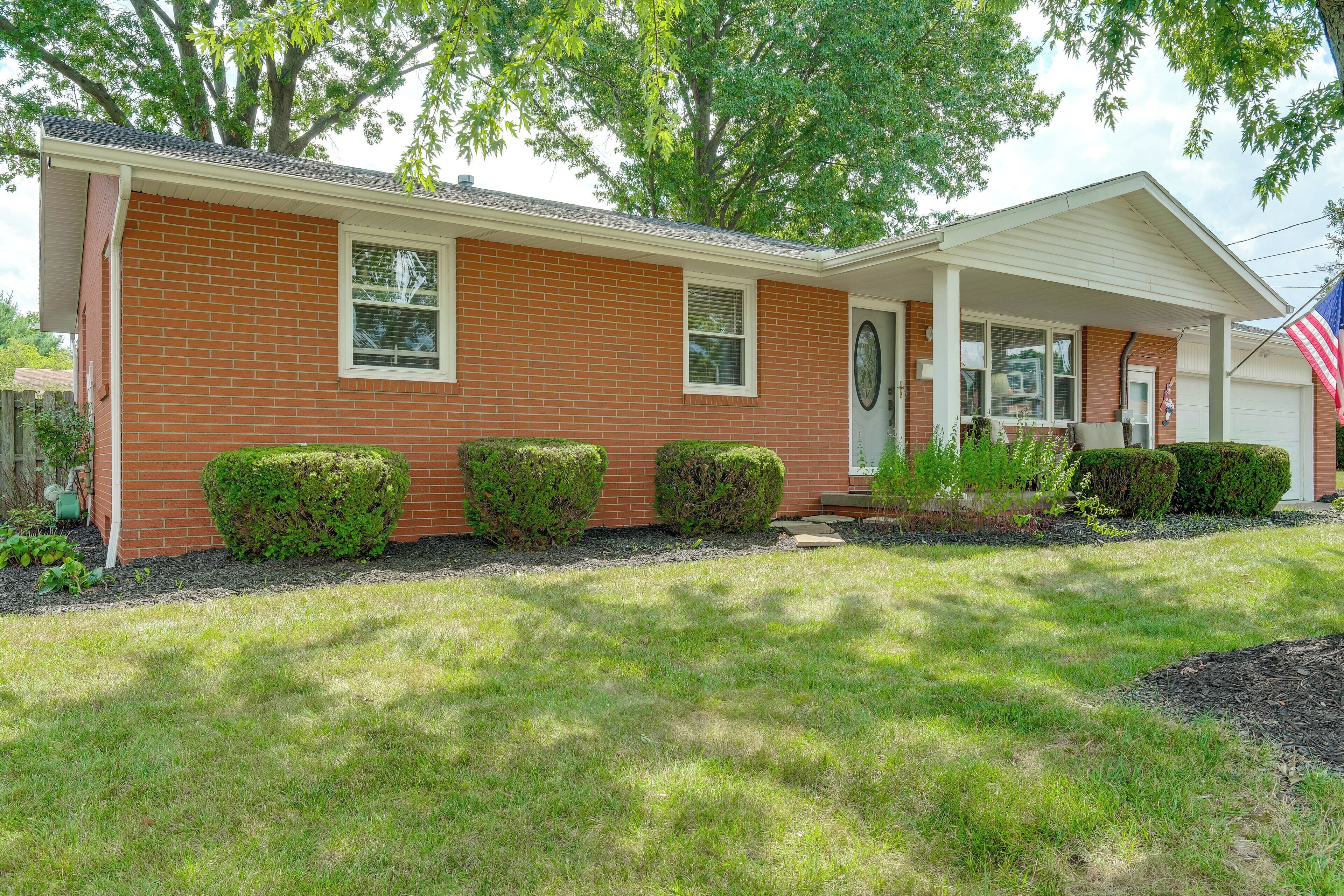 A single-story brick house with a front porch, a garage, and a well-maintained lawn.