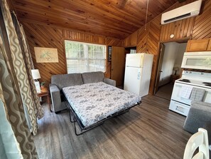 A compact RV interior with a bed, kitchenette, and wooden walls.