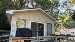 A wooden deck with a covered grill, a dining table with chairs, and a sliding glass door.