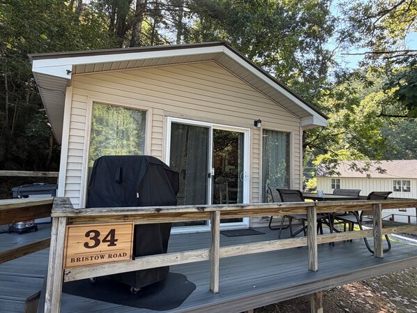 A wooden deck with a covered grill, a dining table with chairs, and a sliding glass door.