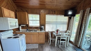 A compact kitchen with wooden cabinets, a microwave, stove, and a dining area with a table and chairs.