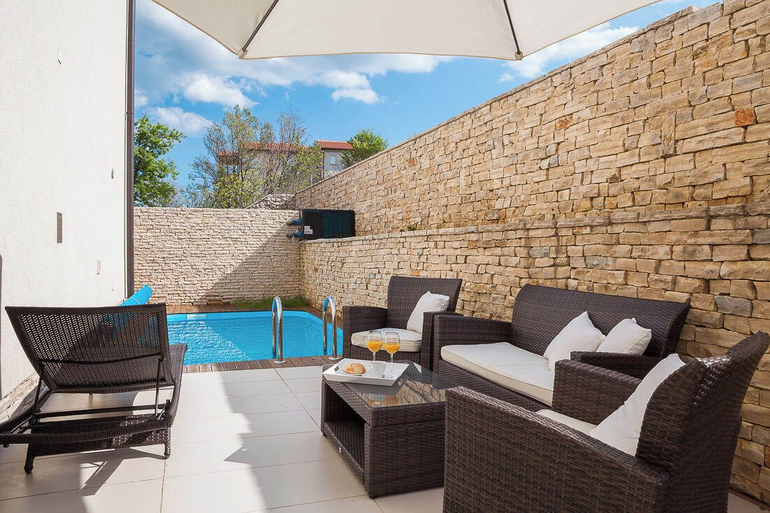 An outdoor seating area with wicker furniture, a pool, and a stone wall.