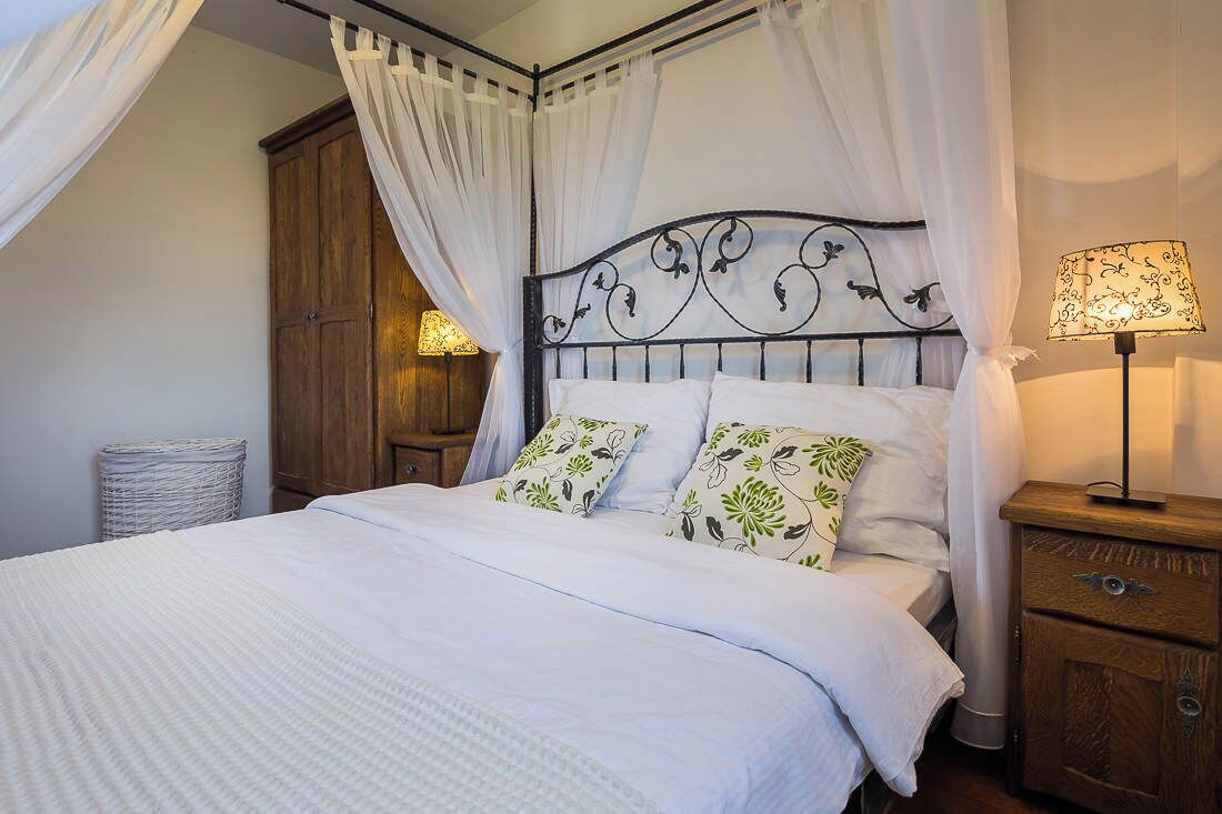 Een bed met baldakijn, een bedlamp en een houten nachtkastje.