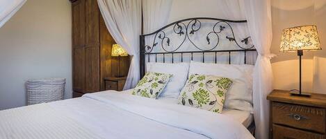 Een bed met baldakijn, een bedlamp en een houten nachtkastje.