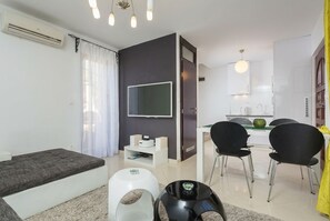 A modern living room with a sofa, a dining area with chairs, a kitchen with cabinets, and a flat-screen TV mounted on the wall. - Villa Olea (Čižići)