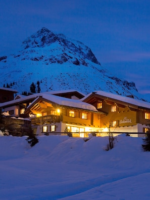 Montanha coberta de neve ao entardecer com um hotel com várias divisões e uma varanda.