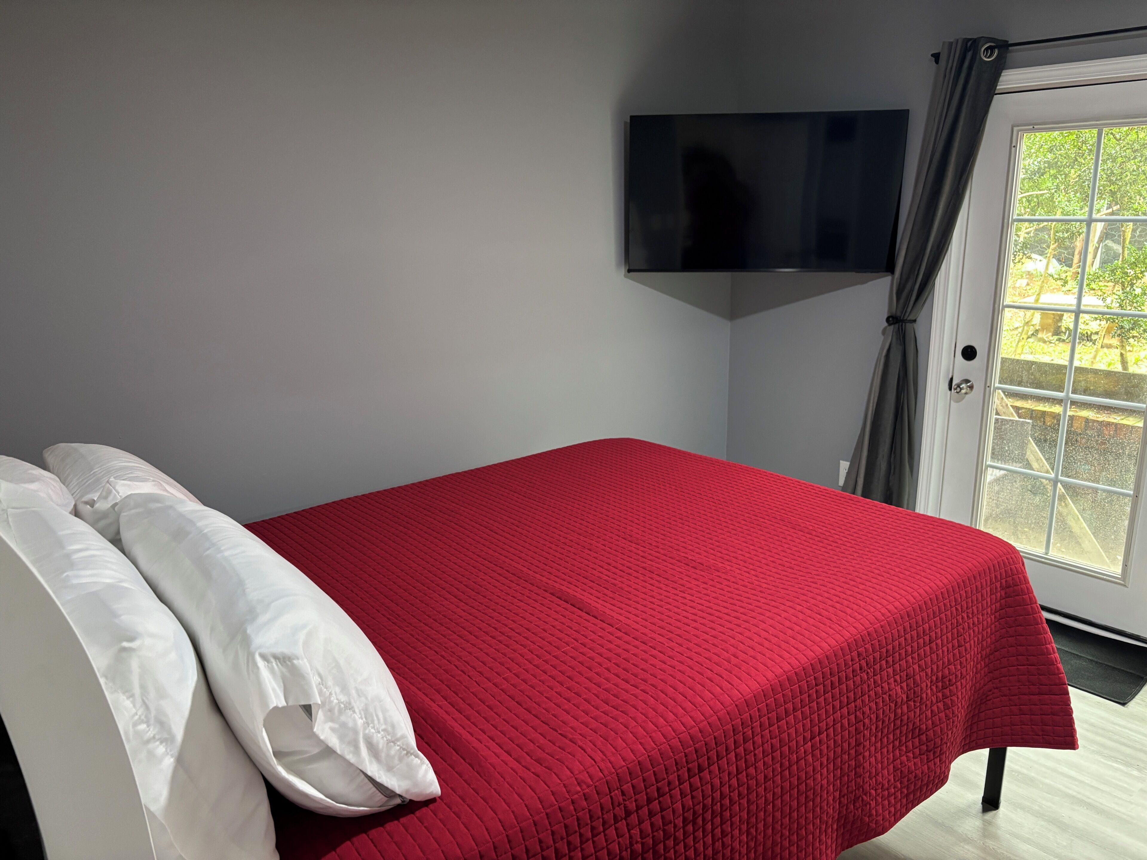 Una habitación con cama, televisor de pantalla plana en la pared y ventana con cortinas.