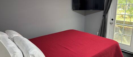 Une chambre avec un lit, un téléviseur à écran plat fixé au mur et une fenêtre avec des rideaux.