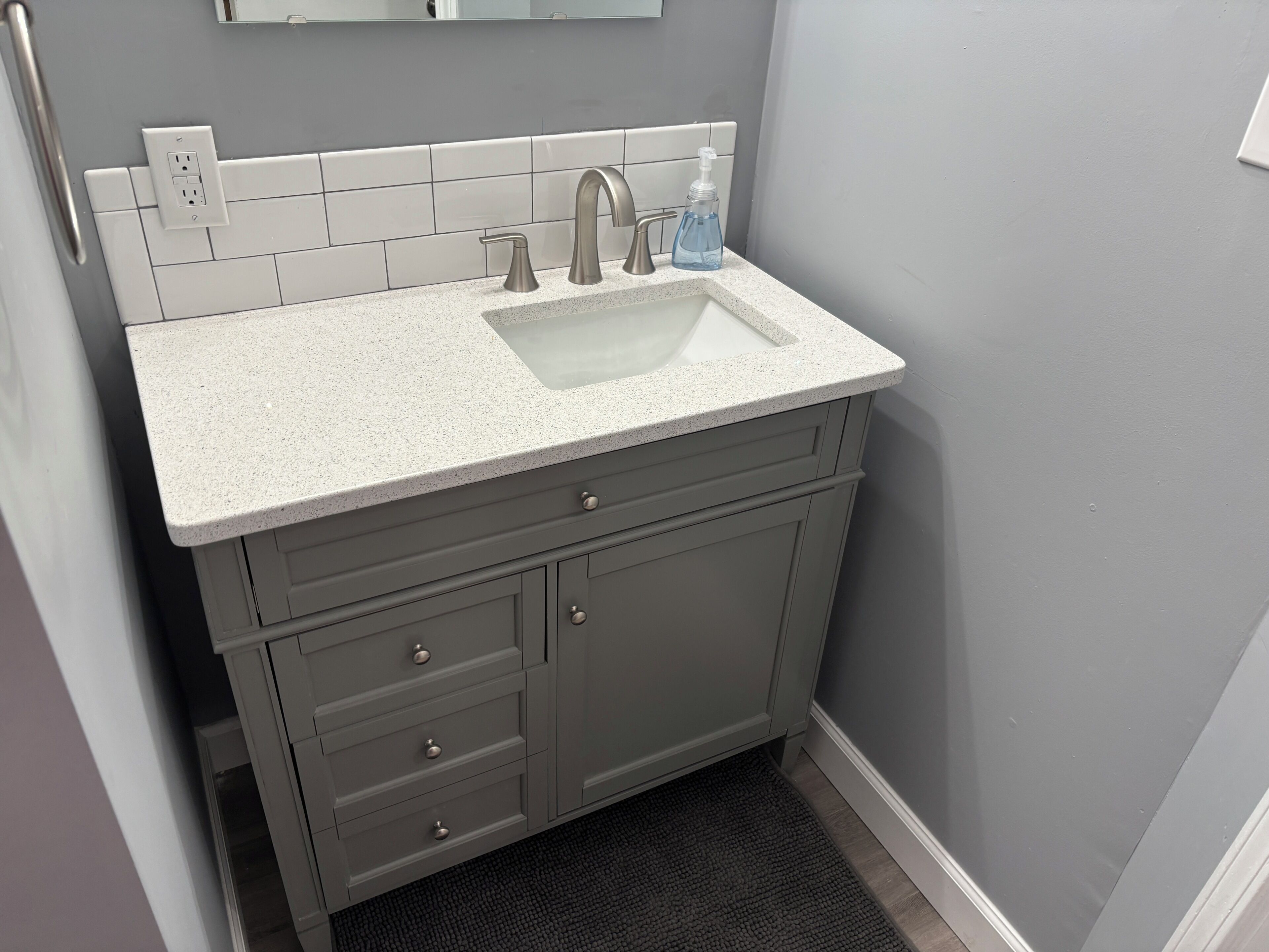 A bathroom with a white sink, grey cabinets, and a small mirror above the mirror.