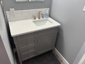 Une salle de bain avec un lavabo blanc, des meubles gris et un petit miroir au-dessus du grand miroir.