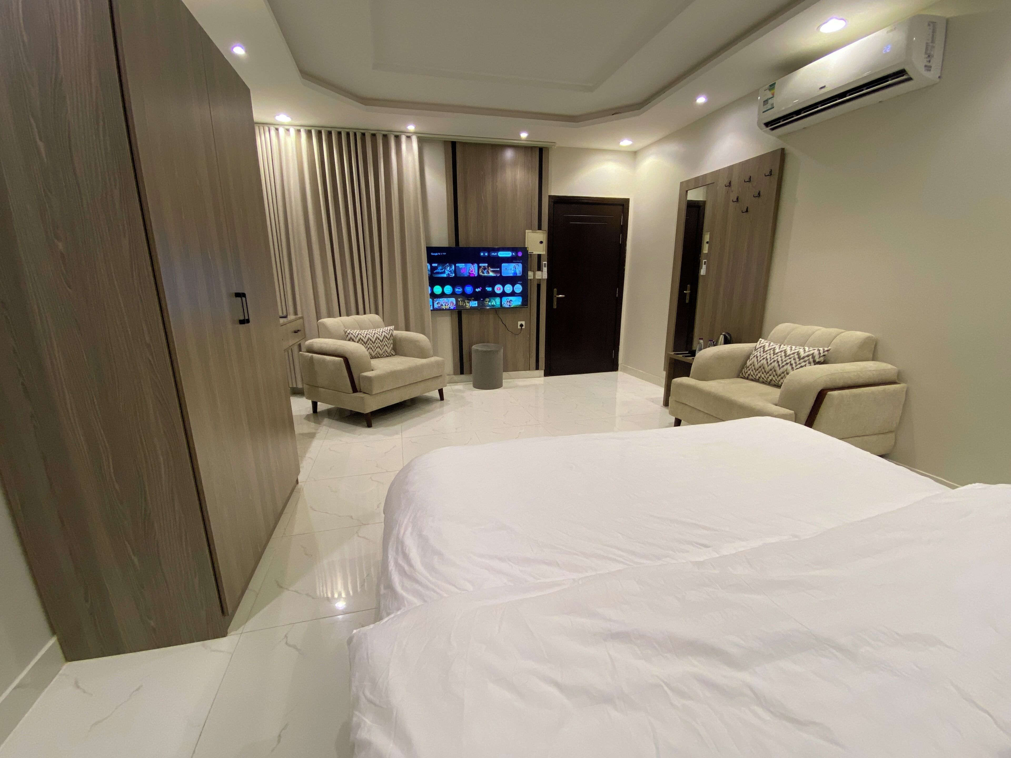 A hotel room with a large bed, two armchairs, a TV, and a wardrobe.