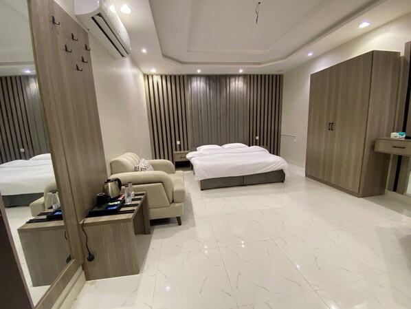 A modern hotel room with a bed, a sofa, a desk with a kettle, and a wardrobe.