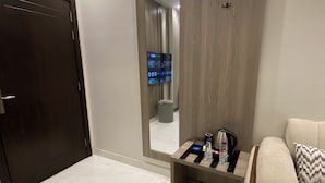 Habitación de hotel con un espejo grande, un sofá, una pequeña mesa con una tetera y una botella, y una puerta.