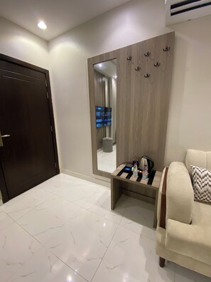 A hotel room with a large mirror, a sofa, a small table with a kettle and a bottle, and a door.