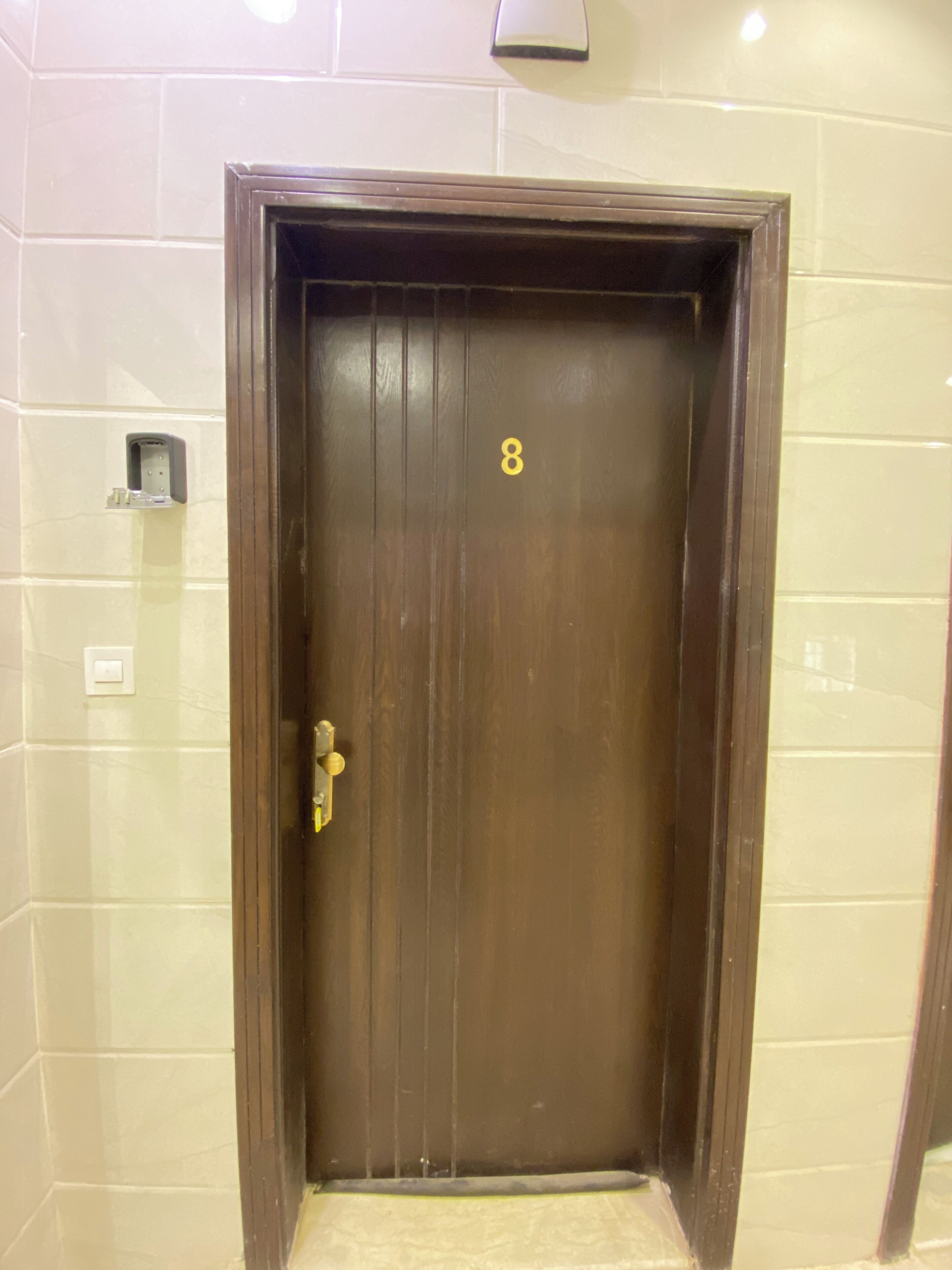 Puerta de madera cerrada con el número 8, un escalón que lleva a ella y un aplique en la pared superior.