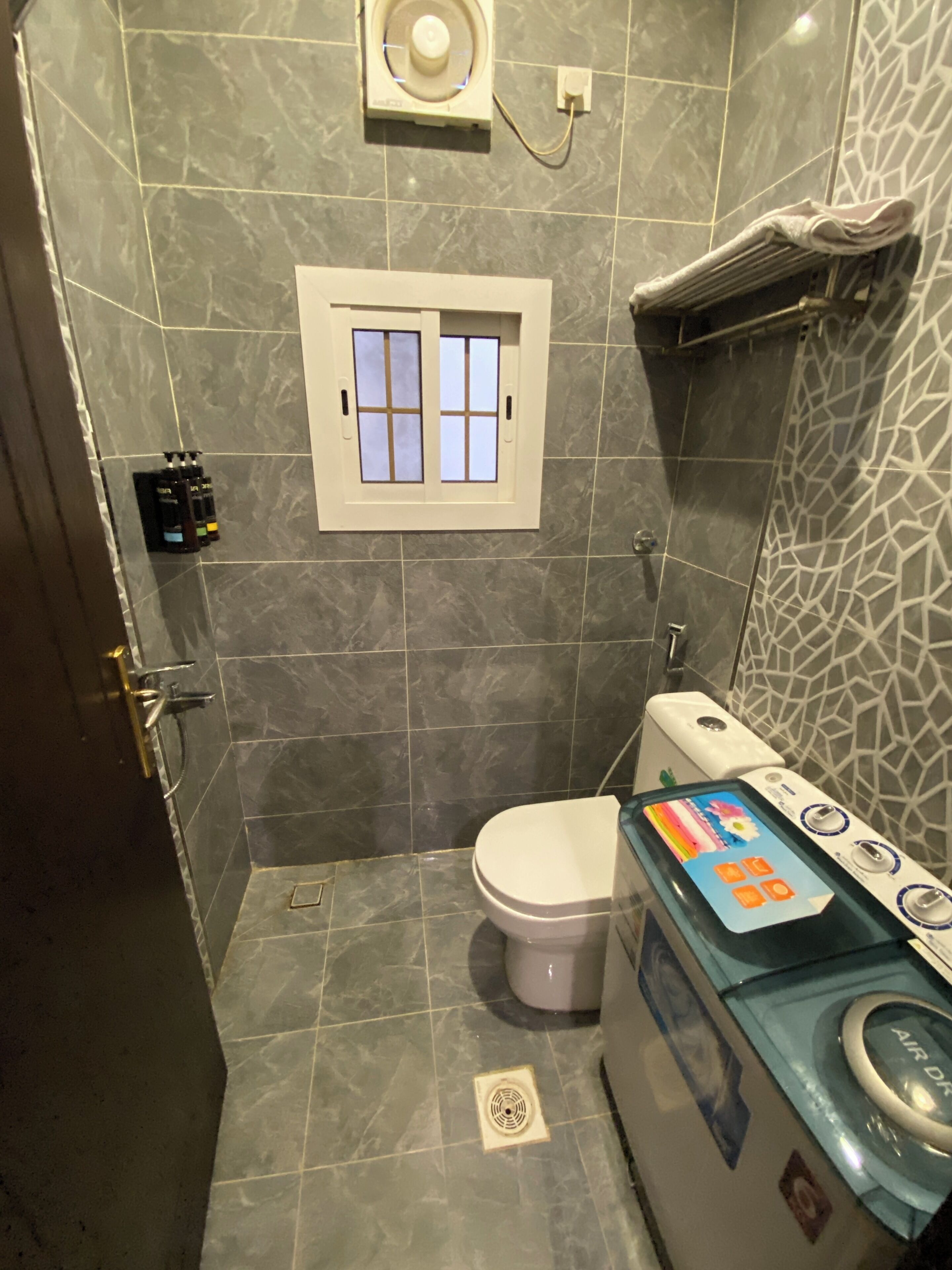 Un baño con inodoro, secador de manos en la pared y lavadora.