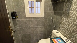 Un baño con inodoro, secador de manos en la pared y lavadora.