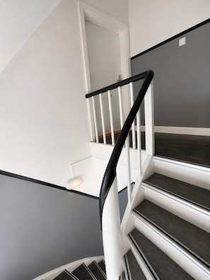 A staircase with white railings and dark steps, leading to a landing with a white wall and a small table.