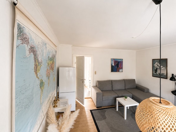 A modern living room with a world map, a grey sofa, a white coffee table, and a hanging lamp.