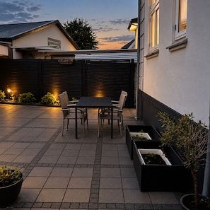 En terrasse med et bord og stole, omgivet af plantekasser og et hegn.