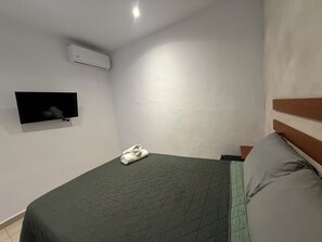 Makuuhuoneessa on sänky, televisio ja seinälle asennettu ilmastointilaite.