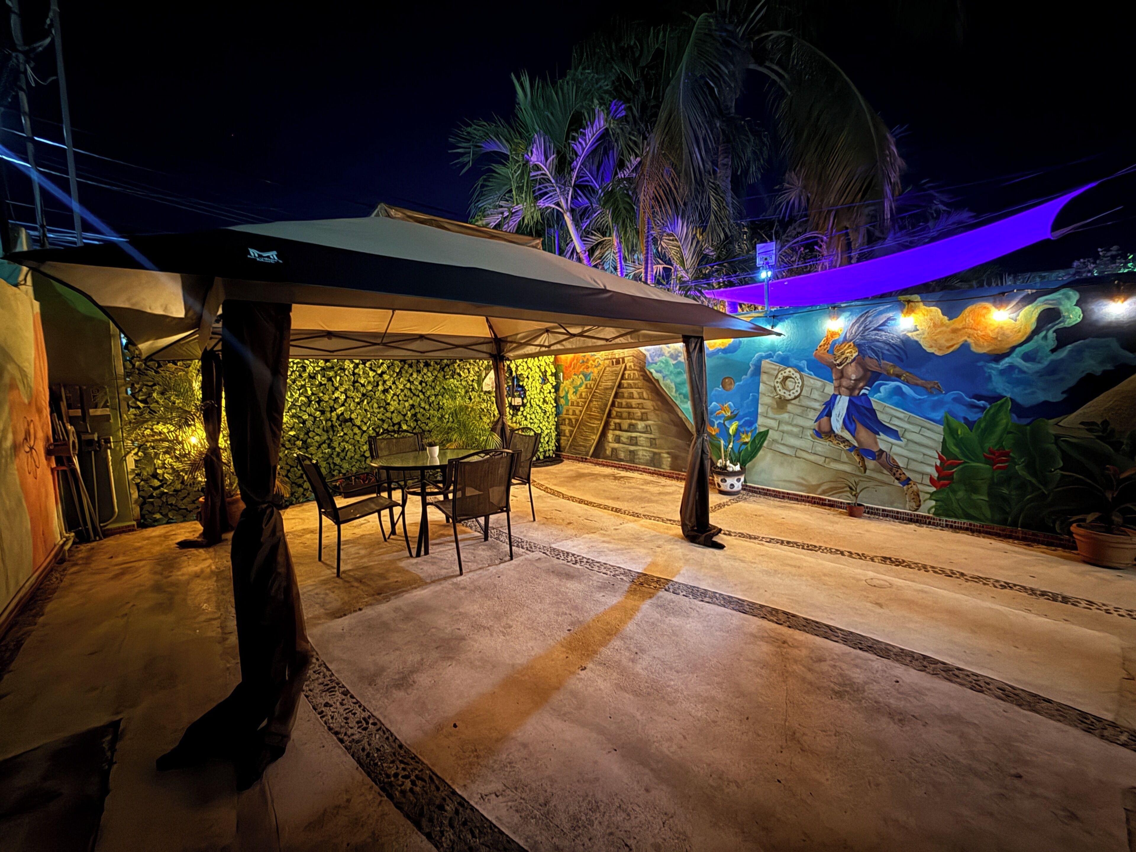 Ein Terrassenbereich im Freien mit überdachter Sitzgruppe und Wandgemälde.