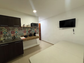 A small kitchenette with a microwave, sink, and cabinets, a television mounted on the wall, and a tiled backsplash. - Casa Villa Leo, Downtown Cancún (Cancún)