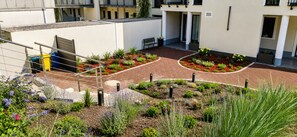 A courtyard with a brick pathway, a metal fence, and various plants.