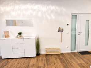 A room with a white cabinet, a small wooden bench, a wall-mounted shelf with a ship model, and a door with frosted glass panels.