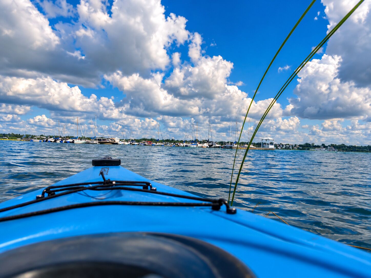 Uitzicht vanaf een boot, met heldere lucht en rustig water, verre gebouwen en boten aan de horizon.