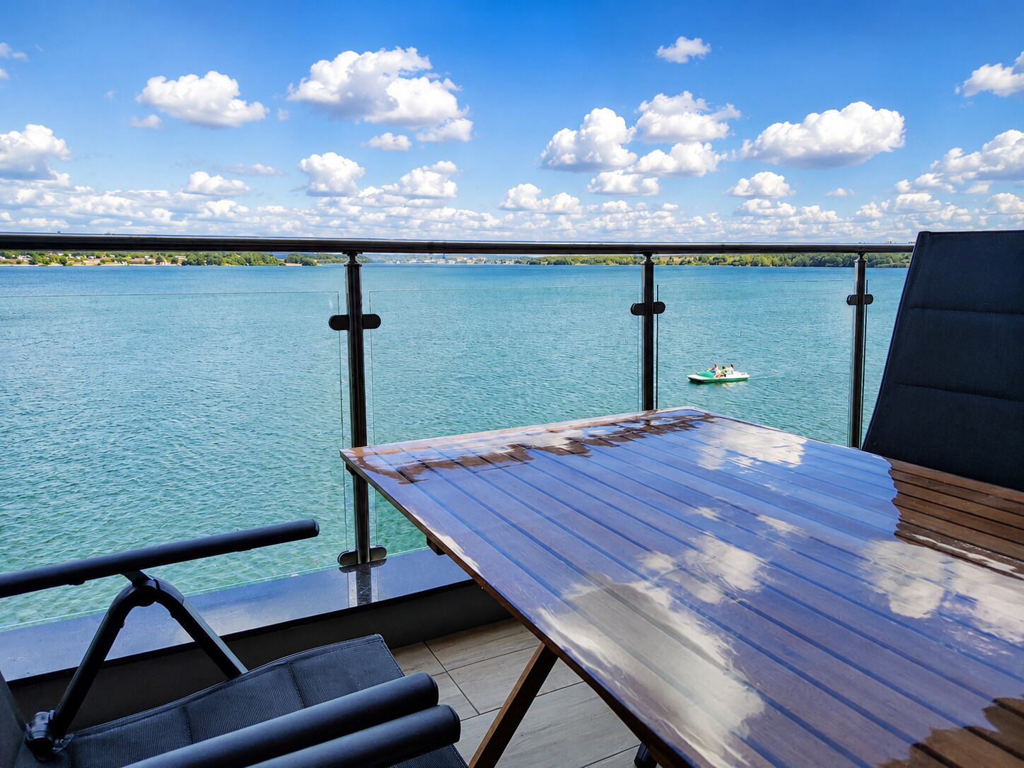 Une terrasse avec une table et des chaises donnant sur une étendue d’eau, avec un bateau visible au loin.