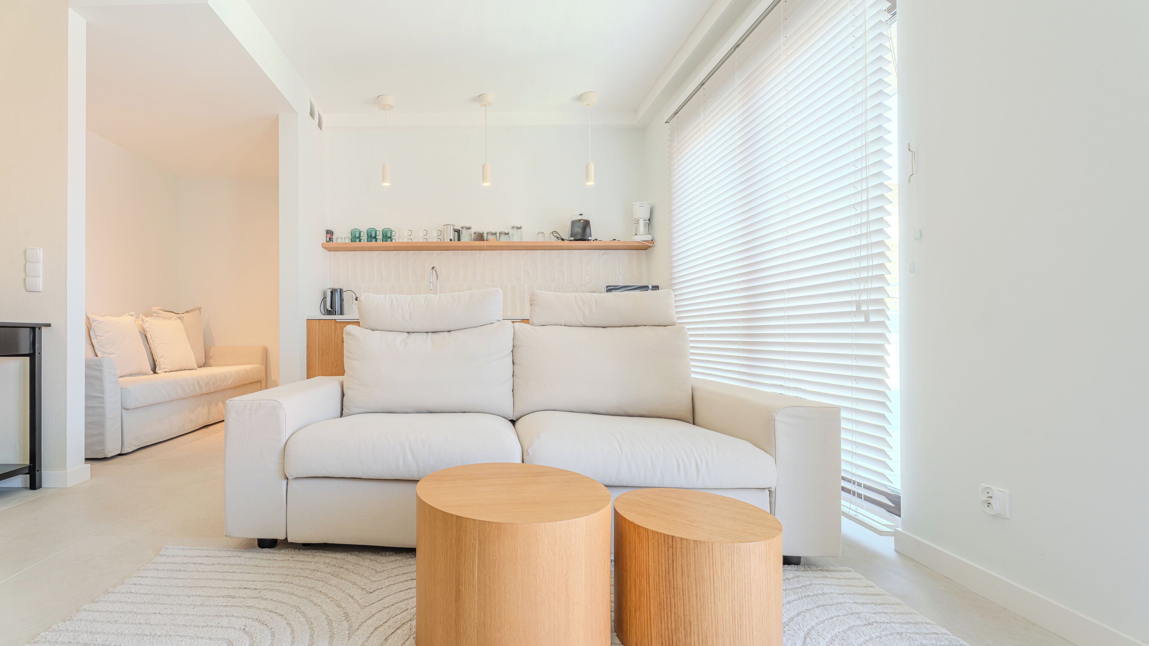 Ein modernes Wohnzimmer mit einer Couch, zwei Holznachttischen und einem Küchenbereich im Hintergrund.