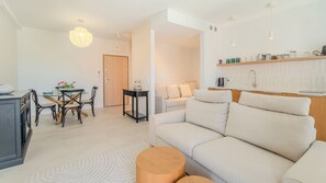 Ein modernes Wohnzimmer mit einer Couch, einem Esstisch und Stühlen. Es gibt eine Küchenzeile mit Arbeitsplatte und Schränken.