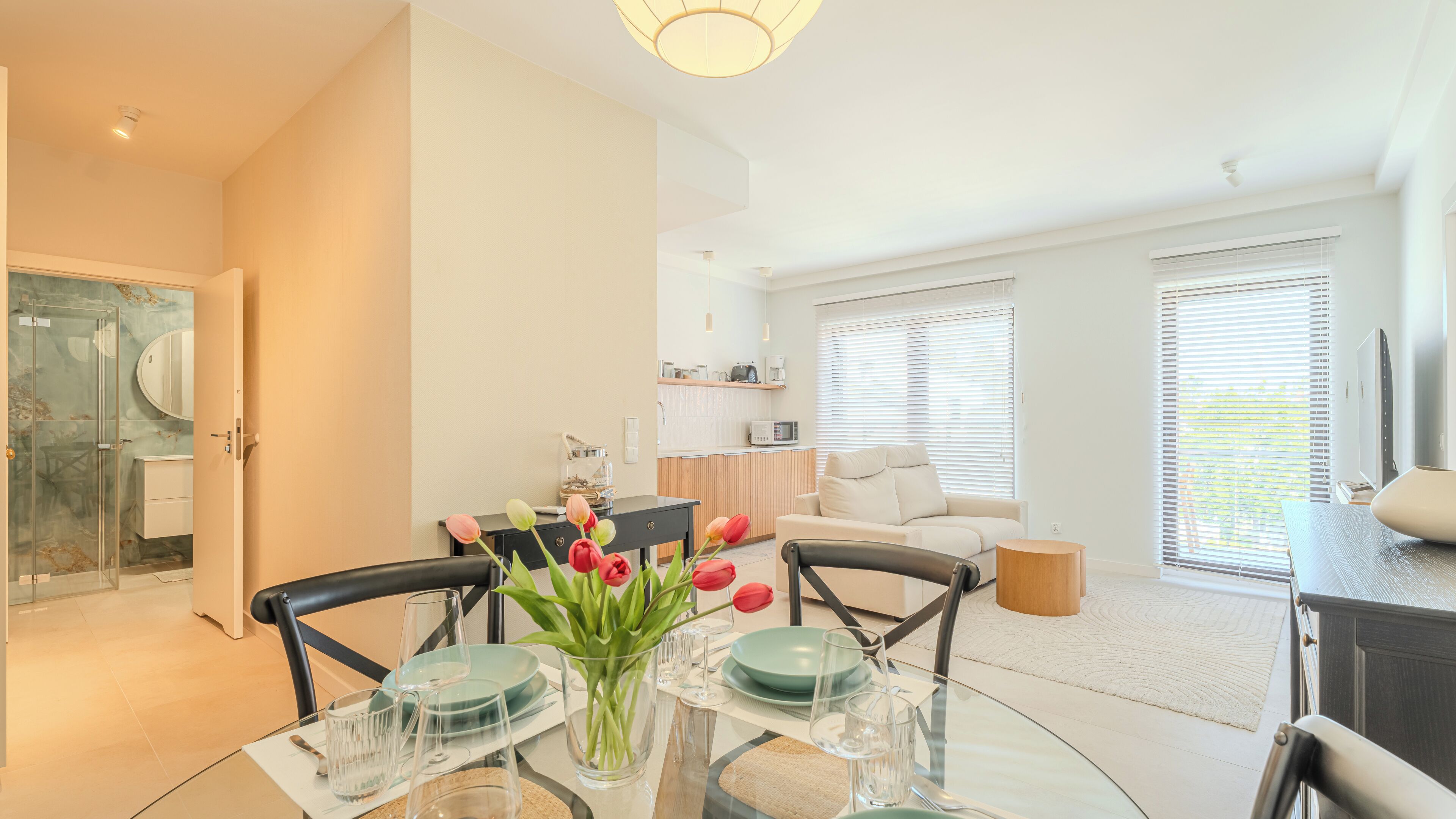 A modern living room with a dining area, a kitchen, and a glass-enclosed shower.