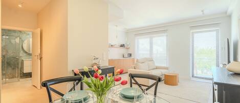 A modern living room with a dining area, a kitchen, and a glass-enclosed shower.
