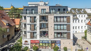 Ein mehrstöckiges Gebäude mit Balkonen, einem Geschäft im Erdgeschoss und einer sichtbaren Straßenszene.