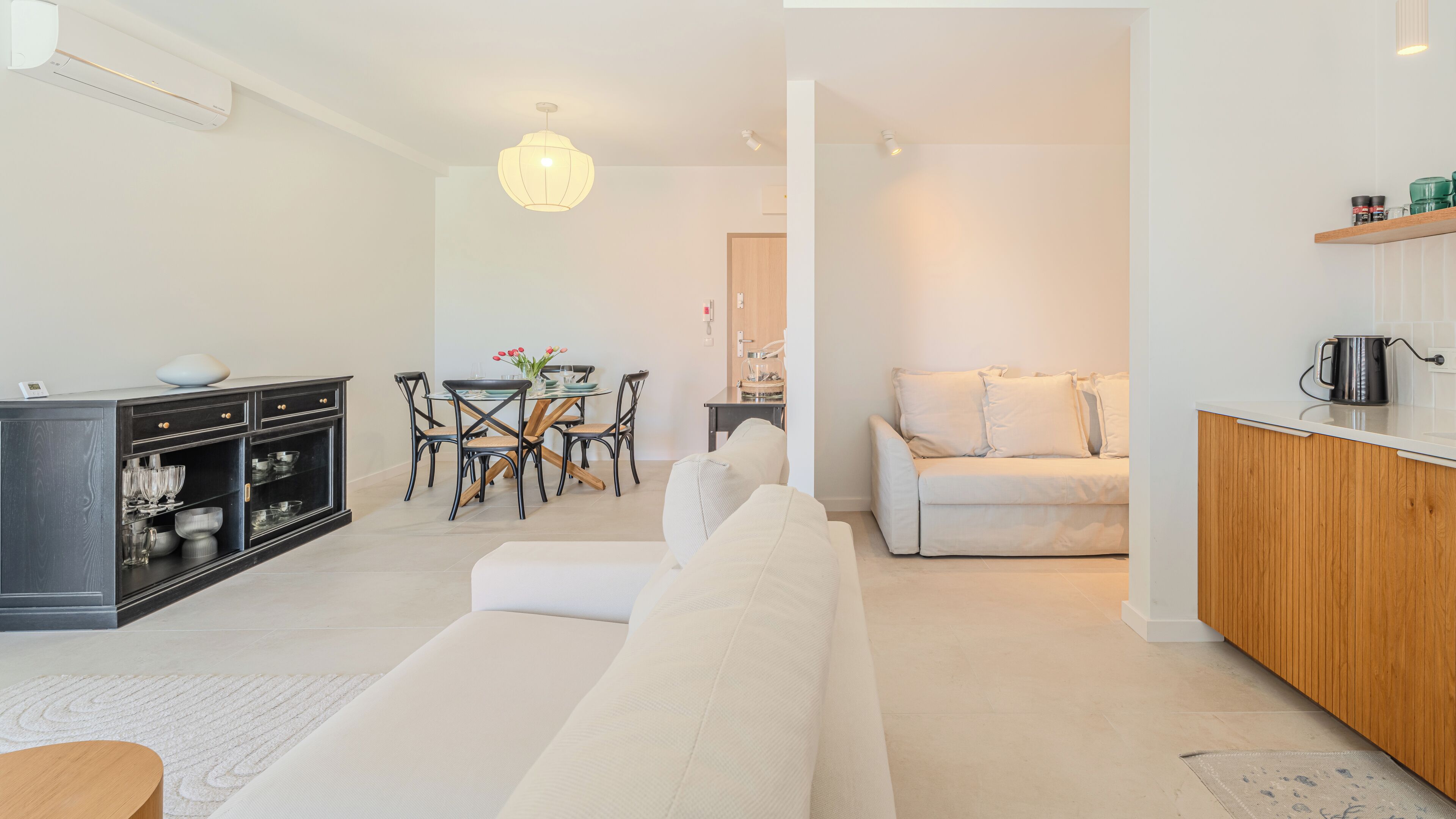 A modern living room with a sofa, dining table, and kitchen area.