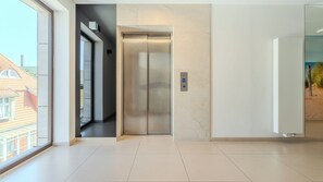 A modern elevator with a digital display, a glass door, and a view of a residential area outside. - Apartamenty Sun & Snow Kormoran (Świnoujście)
