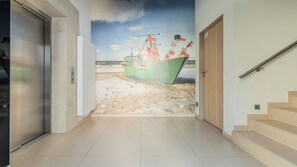 Un couloir orné d’une fresque représentant une scène de plage, avec un escalier et une porte.