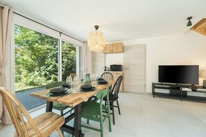 Un espace repas moderne avec une grande fenêtre, une table à manger dressée avec des assiettes et des verres, un téléviseur et un four à micro-ondes.