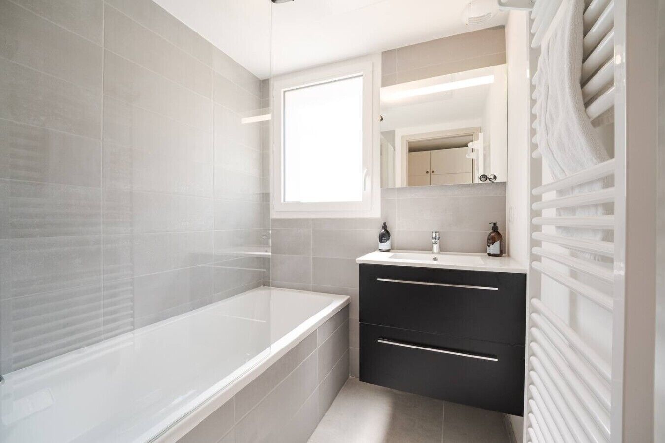 A modern bathroom with a bathtub, a vanity with a mirror, and a towel rack.