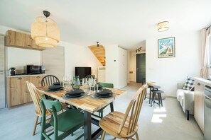 A modern kitchen with wooden cabinets, a dining table set for four, and a hanging light fixture. - Cimes - Cozy Apartment | 5 guests | Family-friendly | Quiet (Chamonix)