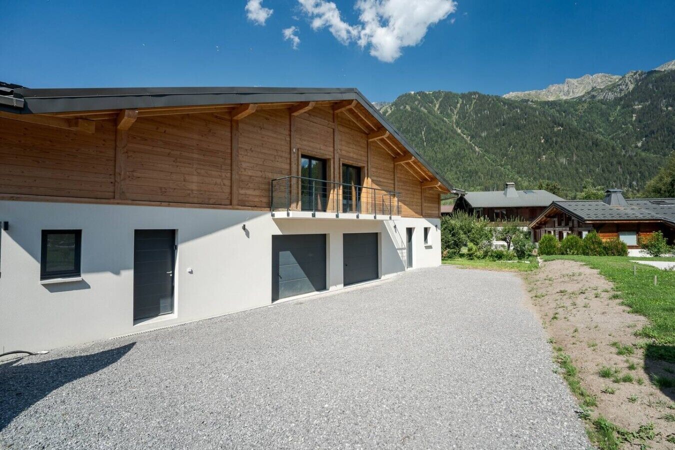 Un edificio moderno con fachada blanca y estructura superior de madera, con montañas al fondo.